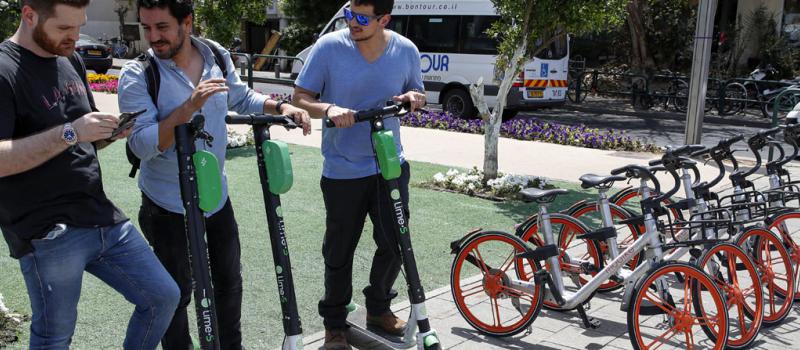 Tres hombres se alistan a utilizar sus monopatines eléctricos, en las calles de Tel Aviv, en Israel.